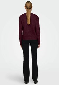 Suéter de punto burdeos con cuello redondo, mangas largas y dobladillo acanalado, combinado con pantalones negros de campana. Textura suave, diseño casual.