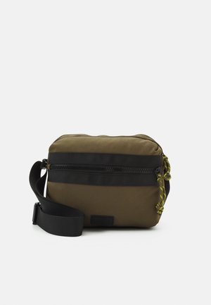 Borsa a tracolla verde oliva realizzata in tessuto resistente. Presenta una chiusura superiore con zip, spallacci neri e un cordoncino decorativo giallo con fermaglio.