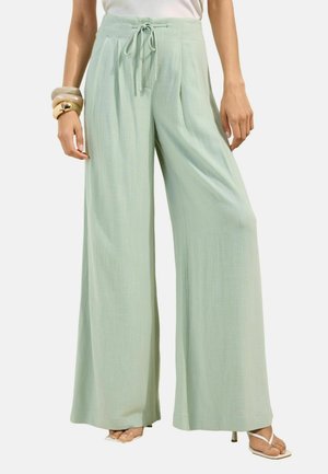 Light green wide-leg pants with a drawstring waist worn with open-toe heels and chunky bracelets on the left wrist.