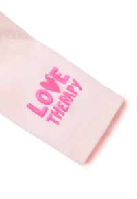 Rosa Langarmshirt mit weichem Stoff, das mit dem gestickten Text "LOVE THERAPY" in leuchtendem Pink versehen ist. Einfaches, lässiges Design.
