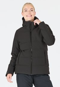 Veste en duvet noire avec fermeture éclair, col montant et capuche ajustable. Dispose de poches latérales zippées et d'une texture matelassée.