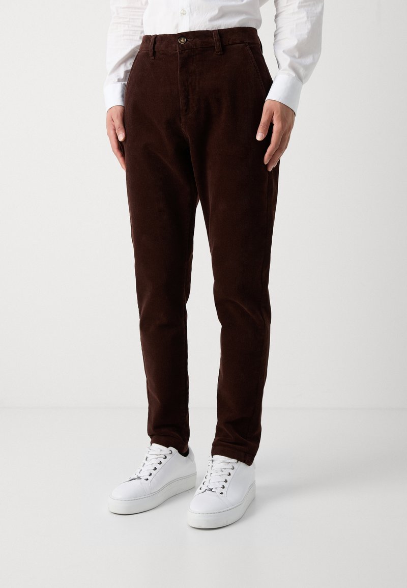 Bruna kordbyxor med rak skärning, med en knappstängning, bältesöljer och sidofickor, kombinerat med vita sneakers.