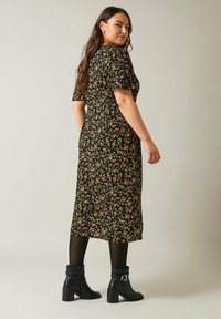 Vestito floreale nero con maniche corte, elastico in vita e lunghezza fino al polpaccio. Indossato con stivaletti neri con tacco.