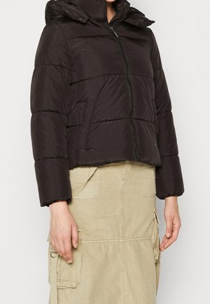 Doudoune noire avec fermeture éclair à l'avant et poignets élastiques portée sur une jupe cargo beige avec plusieurs poches et détail anneau.