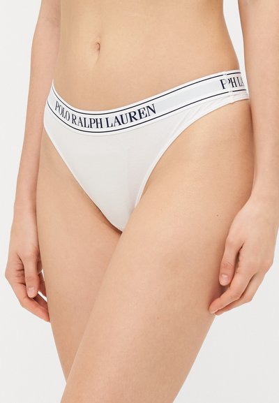 Balta stringu apakšveļa ar tumši zilu logotipa joslu, uz kuras rakstīts "POLO RALPH LAUREN." Gluda tekstūra, minimāla seguma līmenis un zema jostasvietas dizains.
