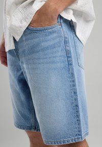 Light blue denim shorts with a relaxed fit, featuring side pockets and a smooth texture. Distressed detailing enhances the casual look.