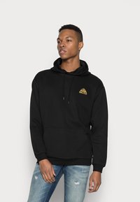 Sudadera negra de mezcla de algodón, con un bolsillo tipo canguro y un logo triangular dorado en el pecho. Puños y bajo de canalé.