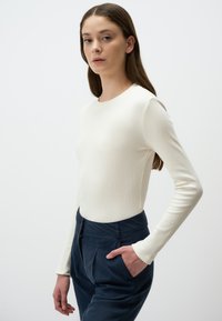 Maglia a maniche lunghe a costine in bianco sporco, abbinata a pantaloni blu scuro a vita alta con tasca laterale e frontale piatto.