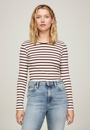 Maglietta a maniche lunghe a righe in materiale a costine bianco e bordeaux, abbinata a jeans in denim azzurri a vita alta.