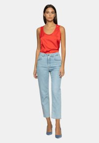 Top rosso senza maniche, jeans azzurri a vita alta, orlo sfrangiato, tacchi alti blu. Design semplice, texture liscia, tessuto leggero.