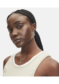 Zilveren oorbellen met een geometrische diamantvorm, gedragen met een zilveren kettinghalsband, tegen een neutrale achtergrond. Huidtint is diep.