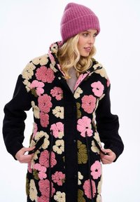 Farebný fleecový kabát s kvetinovým vzorom na čiernom pozadí, s vysokým golierom, prednými vreckami a textúrovaným povrchom.