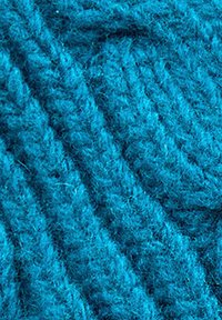 Filato turchese con una texture morbida e pelosa. Presenta un motivo intrecciato con spesse trefoli intrecciati.