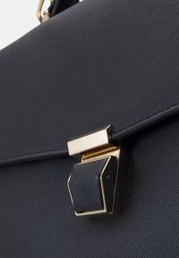 Sac à main noir texturé avec un fermoir en métal doré, au design angulaire et accents lisses. La surface présente une finition à motifs subtils.