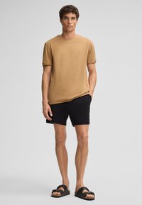 Tanjacket met ronde hals, korte mouwen, relaxte pasvorm, gecombineerd met zwarte shorts en zwarte slidesandalen. Casual stoftextuur, minimalistisch design.