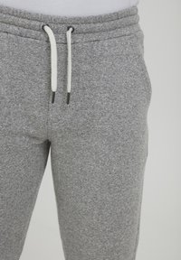 Gray cotton sweatpants with elastic waistband, white drawstrings, and a textured surface. Close-up view of the lower half of the garment.