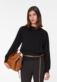 Zwarte gebreide trui met een ribbelrand, voorzien van gouden accenten op de kraag. Bruine gestructureerde handtas met een trekkoord en kettingdetails.