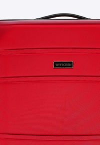 Maleta roja hecha de material texturizado con un acabado suave, que presenta herrajes negros y una placa de logo de la marca en la parte frontal.