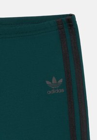 Teal träningsbyxor med svarta sidostripes och en diskret grå Adidas-logotyp. Tillverkade av mjuk, stretchig tyg för komfort.