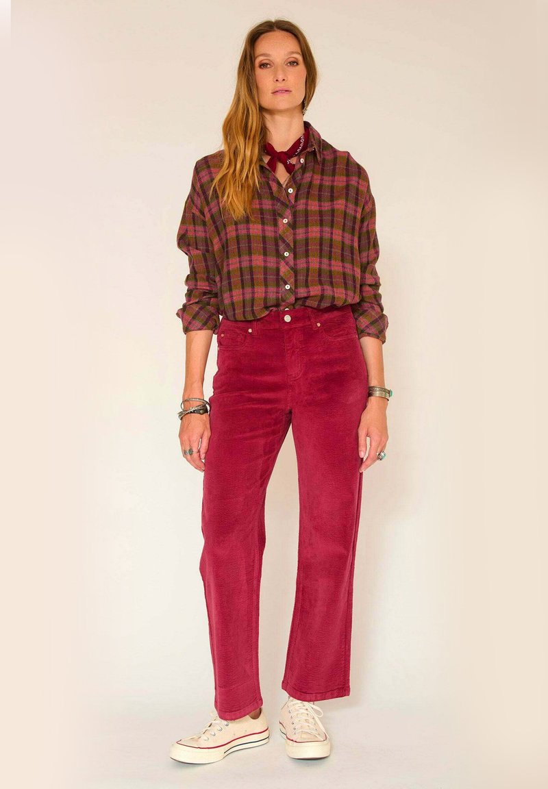 Chemise à carreaux avec des boutons en vert et bordeaux, associée à un pantalon bordeaux en velours côtelé taille haute et des baskets blanches.