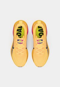 Κίτρινα παπούτσια τρεξίματος με άνω μέρος από δίχτυ, μοβ λεπτομέρειες και μαύρο λογότυπο. Μαλακή σόλα με έντονα γράμματα "RUN" και "ROAD" στις εσωτερικές σόλες.