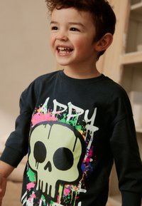 Felpa nera con grande grafica verde di un teschio e accenti di schizzi colorati. Collo e polsini a coste, vestibilità comoda, materiale in cotone.