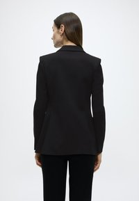 Μαύρο σακάκι με ραφές, με δομημένους ώμους και φαρδιά κάτω άκρη, με λεία υφή και μονή πίσω σχισμή.