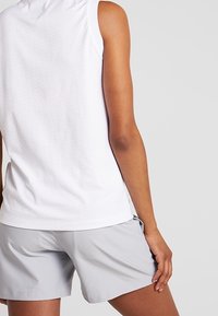 Haut de sport blanc sans manches avec un motif texturé, associé à un short gris clair. Accent sur la douceur du tissu et la coupe ajustée.