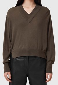 Brązowy sweter z dekoltem w serek, długimi rękawami, ściągaczami na mankietach i u dołu, wykonany z miękkiego materiału, w połączeniu z czarnymi skórzanymi spodniami.