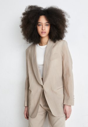 Beige linen blazer with a notched lapel, one button closure, and two front pockets; smooth texture with subtle creases, tailored fit.