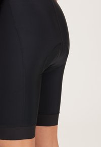 Schwarze sportliche Shorts mit einer glatten, dehnbaren Textur, die eine Länge bis zur Mitte des Oberschenkels und eine eng anliegende Passform aufweisen. Auffällige verstärkte Nähte und keine Muster.