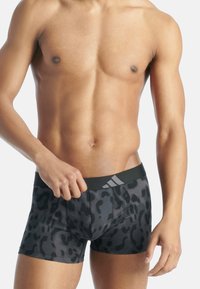 Černé boxer šortky s leopardím potiskem a černým pasem se třemi šedými pruhy. Tkanina vypadá hladce a přiléhavě.