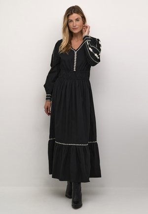 Rochie maxi neagră cu mâneci lungi, talie elastică, decolteu în V și cusături decorative albe pe margini. Material texturat și tiv evazat.