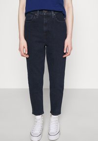 Mörkblå denimjeans med hög midja, slim fit, femficksdesign och subtila sömdetaljer, kombinerat med vita hög toppen sneakers.