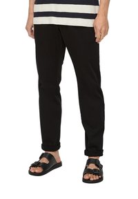 Pantalones negros con dobladillos acampanados, combinados con sandalias negras que cuentan con una correa y detalle de hebilla. La parte superior tiene rayas horizontales en azul marino y blanco.