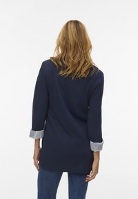 Mornarica blazer izdelan iz mehkega materiala, z zavihanimi črtastimi manšetami in prilegajočim krojem, ki sega do sredine stegna.