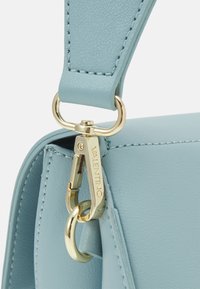 Světlomodrá kožená kabelka s prvky ze zlatého kovu, výrazným zapínáním na klip a detailním prošíváním podél popruhu a těla kabelky.