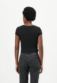 Black cropped T-shirt with short sleeves, round neckline, ribbed texture. Paired with high-waisted dark gray jeans and visible back pockets.