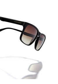 Mustat aurinkolasit, joissa liukuvärjätyt linssit tummanruskeasta vaaleanruskeaan. Mattapintaiset, kultainen "HAWKERS"-logo sankoissa. Suorakaiteen muotoiset.