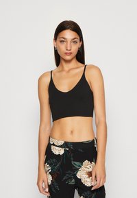 Svart crop-top med tunna axelband och djup halsringning. Bärs med blommig hög midjebyxor som har stora krämfärgade och gröna blommor.