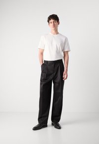 Weißes Baumwoll-T-Shirt, schwarze plissierte Hose und schwarze Schuhe. Einfaches Design mit einer lockeren Passform, glatter Textur und klassischen Farben.