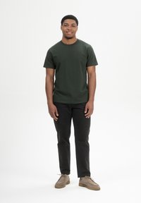 Donkergroene T-shirt met korte mouwen, zwarte broek en beige schoenen. Eenvoudig ontwerp met een ronde hals, casual pasvorm, gladde stofstructuur.