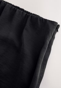 Černý látkový obal se shromážděným horním dílem a zipem, položený na bílém povrchu.