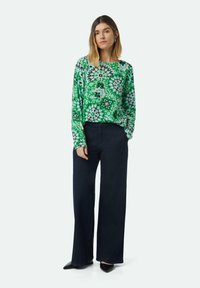 Groene bloemenpatroon lange mouwen top met een losse pasvorm, gecombineerd met hoge taille donkere denim wijde broek en zwarte puntige schoenen.