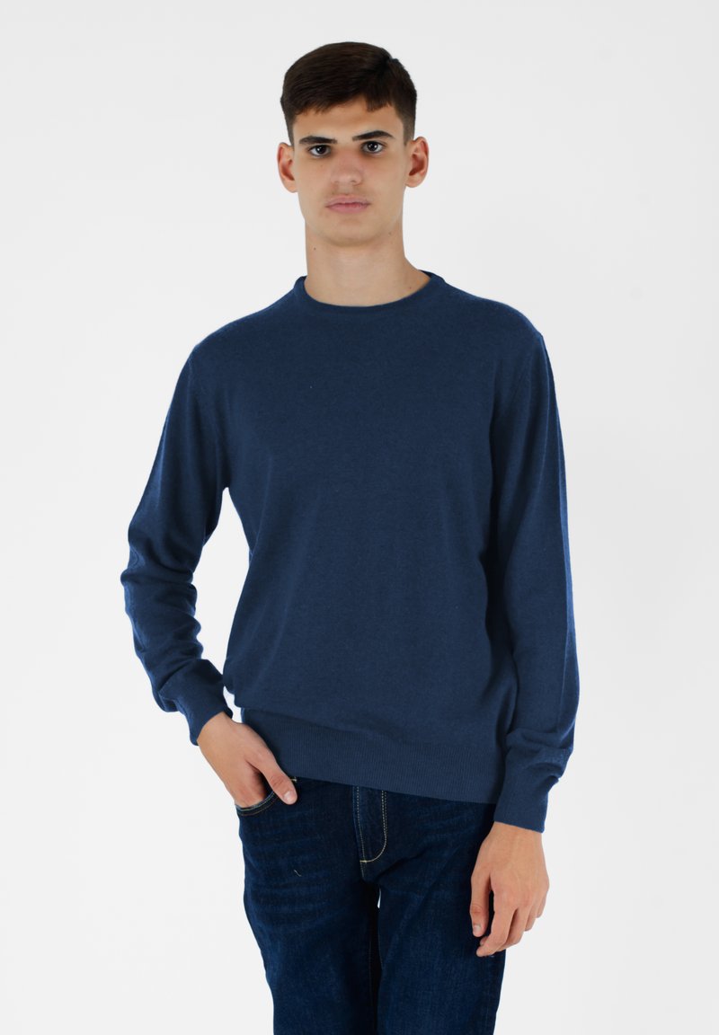 Granatowy sweter wykonany z miękkiego materiału, z okrągłym dekoltem, długimi rękawami oraz ściągaczami przy mankietach i u dołu. Noszony z ciemnymi dżinsami.