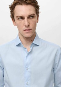 Camicia azzurra chiaro con un sottile motivo a righe; presenta un colletto classico, maniche lunghe e una consistenza liscia e morbida.