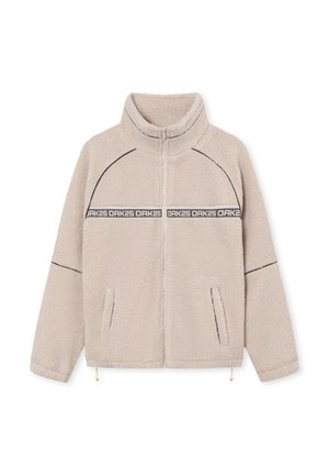 Veste en polaire beige avec un col montant, fermeture éclair, poches latérales et coutures noires contrastantes. Présente une bande logo sur la poitrine.