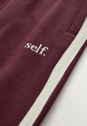 Bordeaux broek met witte zijstrepen en geborduurd logo "self." nabij de zak. Zacht materiaal met een gladde textuur.