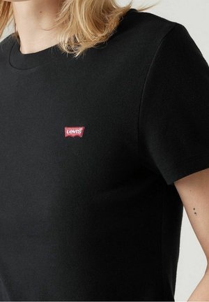 Zwart T-shirt met korte mouwen en een klein rood Levi's-logo op de linkerborst, gedragen door een persoon met lichtblond haar.