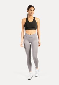 Reggiseno sportivo nero e leggings grigio chiaro, caratterizzati da una texture liscia e un design aderente, abbinati a scarpe da ginnastica bianche.